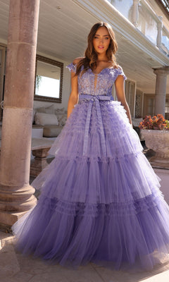 A woman stands outdoors beside a stone column in the Nox Anabel Designer Ruffled Prom Ball Gown E1293, a floor-length lavender tulle dress with beaded embroidered lace and a deep V-neck.