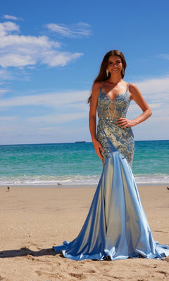 A woman wearing the Nox Anabel E1532 Long Mermaid Prom Dress, with beaded embroidery in light blue, stands on a sandy beach against a beautiful ocean and sky backdrop.