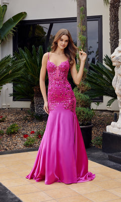 A woman outdoors stands on a tiled patio near greenery and a white statue, wearing the Nox Anabel E1532 Long Mermaid Prom Dress in fuchsia, featuring floral embellishments and beaded embroidery.