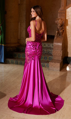 A woman stands indoors in the Nox Anabel E1532 Long Mermaid Prom Dress, a floor-length magenta gown with lace detailing, beaded embroidery, and a low back, facing slightly away from the camera.