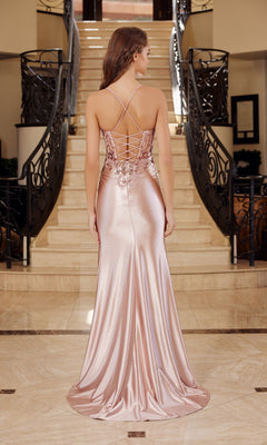 A woman stands on a marble floor before a staircase, wearing the Nox Anabel E1534 Lace-Up Corset Long Prom Dress—a shiny light pink sequin gown with thin straps and a lace-up back.