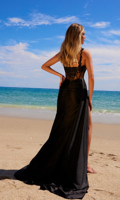 Wearing the Sheer-Waist Long Prom Dress: Nox Anabel E1711, a woman stands on a sandy beach facing the ocean beneath a partly cloudy sky.