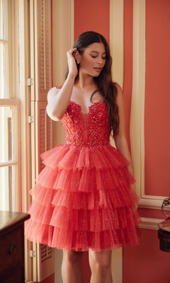 A woman in the Nox Anabel E904 Glitter Babydoll Homecoming Dress stands indoors by a window, touching her ear and looking down.