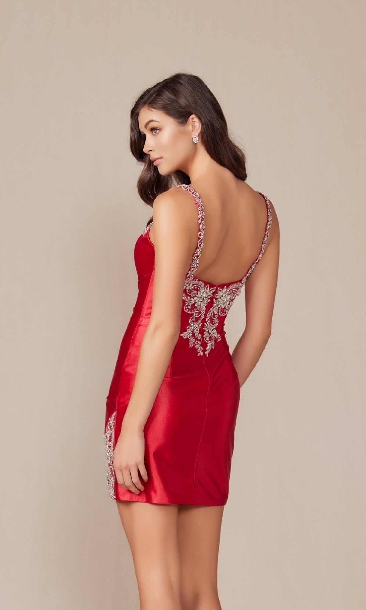 A woman models the Embellished Short Homecoming Dress E912, a red sleeveless, backless cocktail dress with silver embroidery, posing against a plain background and looking over her shoulder.