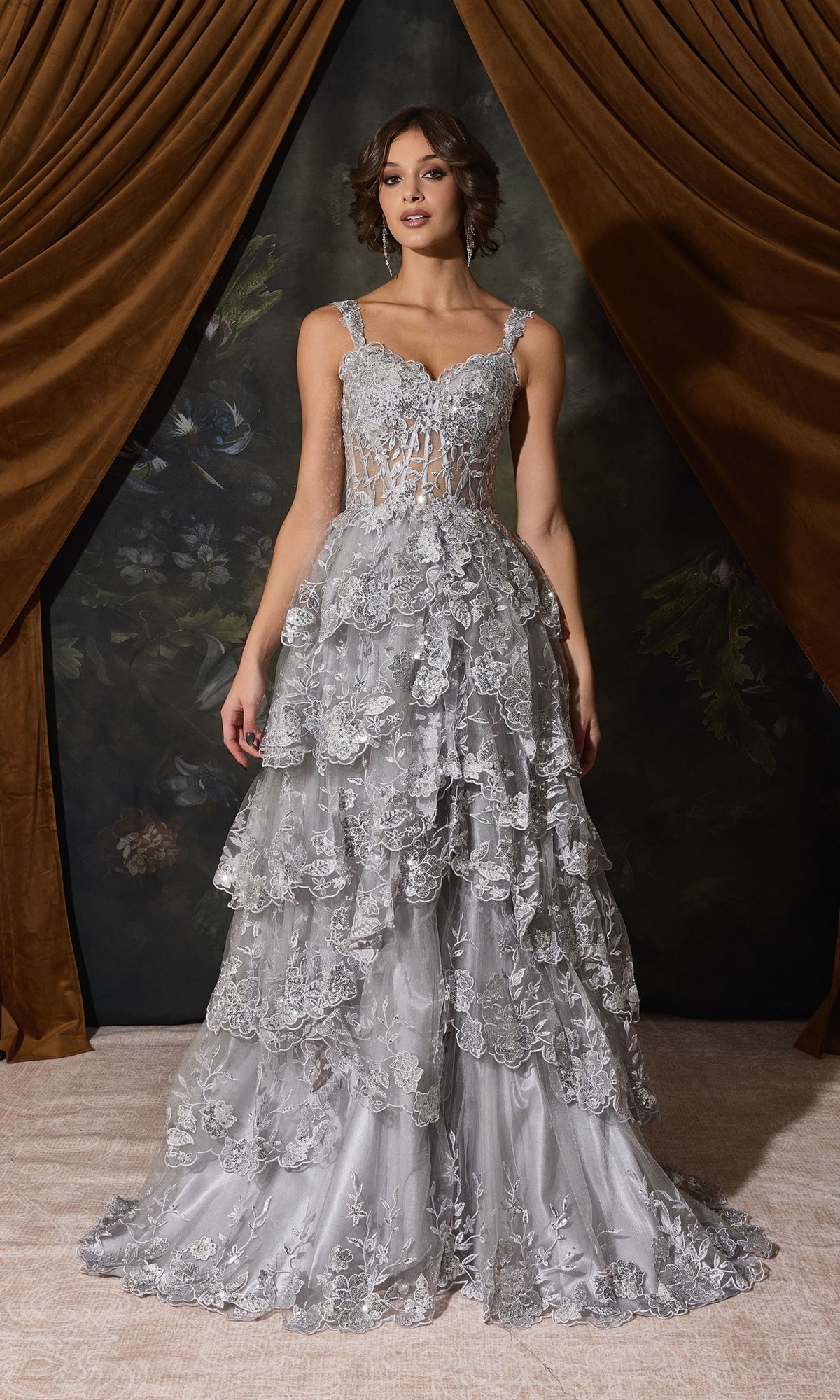 A woman wearing an Off-Shoulder Long Ruffle Prom Dress: Eureka EK102, featuring a floor-length, off-the-shoulder gown with a sheer corset bodice and a silver tiered, floral-embroidered skirt.