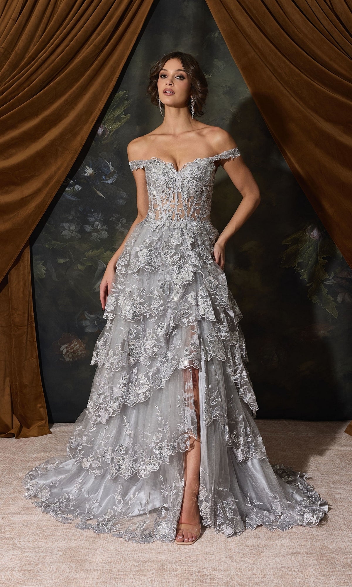 Eureka EK102 off-shoulder, floor-length silver gown with an illusion bodice, floral embroidery, and a layered ruffle skirt for a formal look.