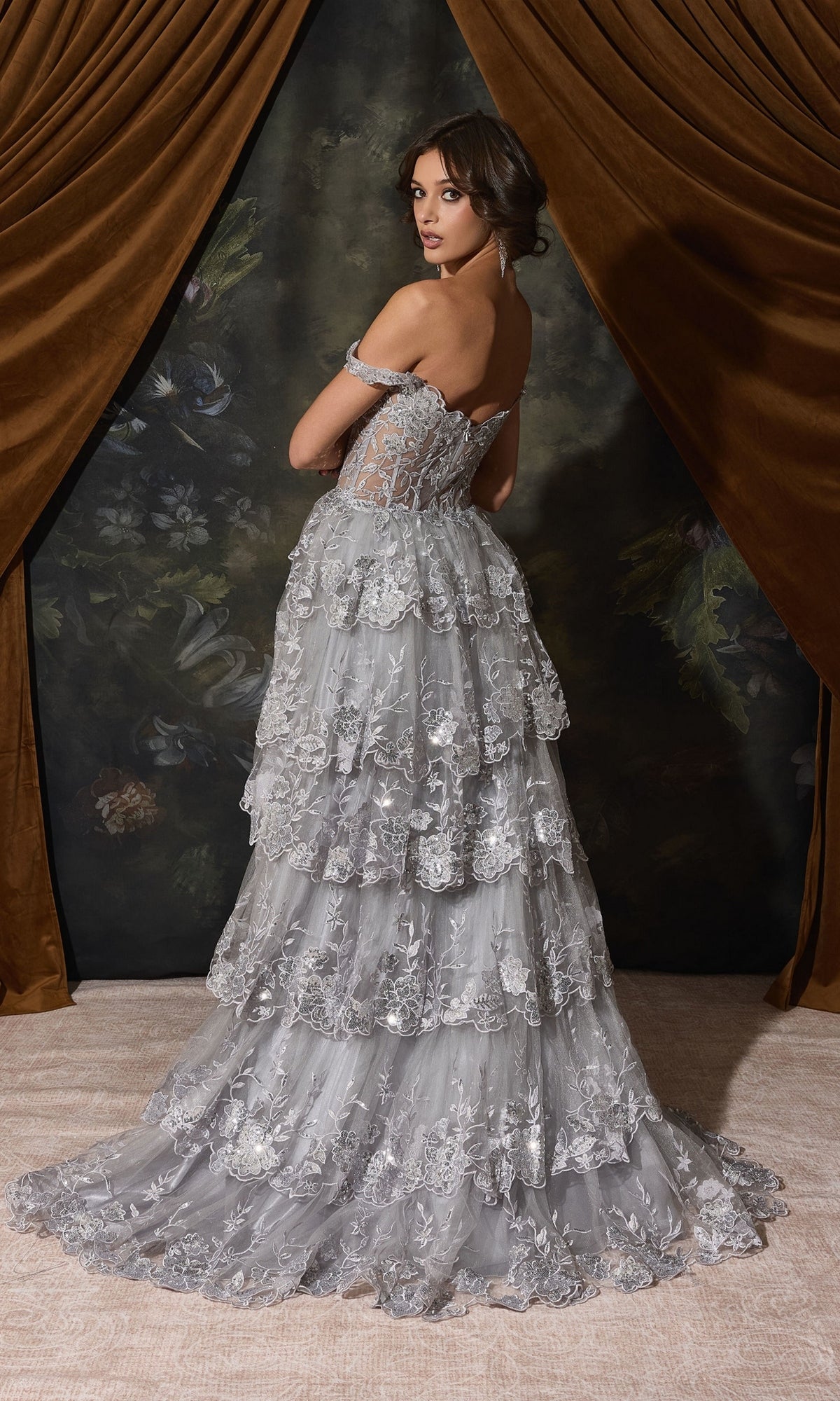 A woman in an Off-Shoulder Long Ruffle Prom Dress: Eureka EK102, a silver, off-the-shoulder, floor-length gown with tiered, lace-embellished ruffled layers and a train.