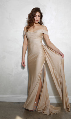 A woman in the Long Ruched Jersey Prom Dress: Eureka EK107 poses against a light textured wall, showcasing the off-the-shoulder design and dramatic thigh-high slit as she holds out part of her evening gown.