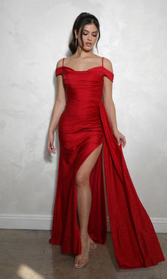 A woman stands gracefully against a light-colored textured wall, wearing the Long Ruched Jersey Prom Dress: Eureka EK107—a fitted red evening gown with an off-the-shoulder neckline and high slit.