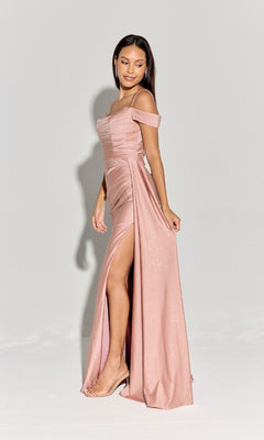 A woman wears the Long Ruched Jersey Prom Dress (Eureka EK107) in shimmery blush pink, featuring an off-the-shoulder neckline and thigh-high slit, as she stands on a light background smiling and glancing to the side.