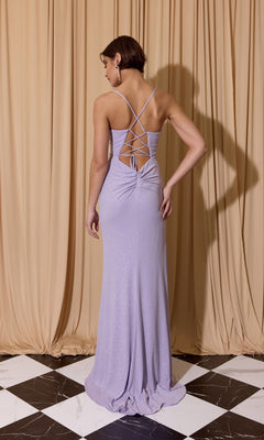 A woman wears the Spaghetti-Strap Glitter Prom Gown: Eureka EK116, a floor-length lavender dress with crisscross straps and an open back, standing on a black-and-white tiled floor before beige curtains.