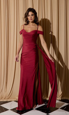 A woman poses gracefully before beige curtains, standing on a black and white tiled floor in the Eureka EK117—a burgundy off-shoulder long formal dress featuring a side slit.