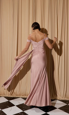 A woman stands with her back to the camera, holding part of the pink Off-Shoulder Long Formal Dress: Eureka EK117, in front of beige curtains on a black-and-white tile floor.