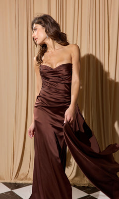 A woman wearing the Strapless Long Satin Prom Dress: Eureka EK118 stands on a black-and-white tiled floor, gently holding her gown, with beige drapes in the background.