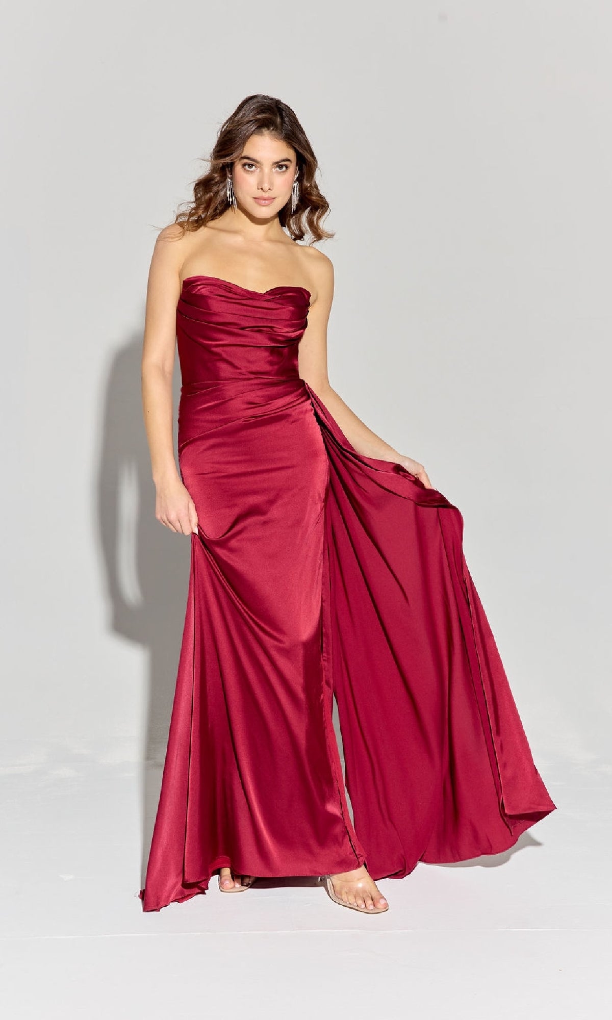 A woman wearing the Strapless Long Satin Prom Dress: Eureka EK118 poses on a plain light background, holding one side of the floor-length skirt away from her body.