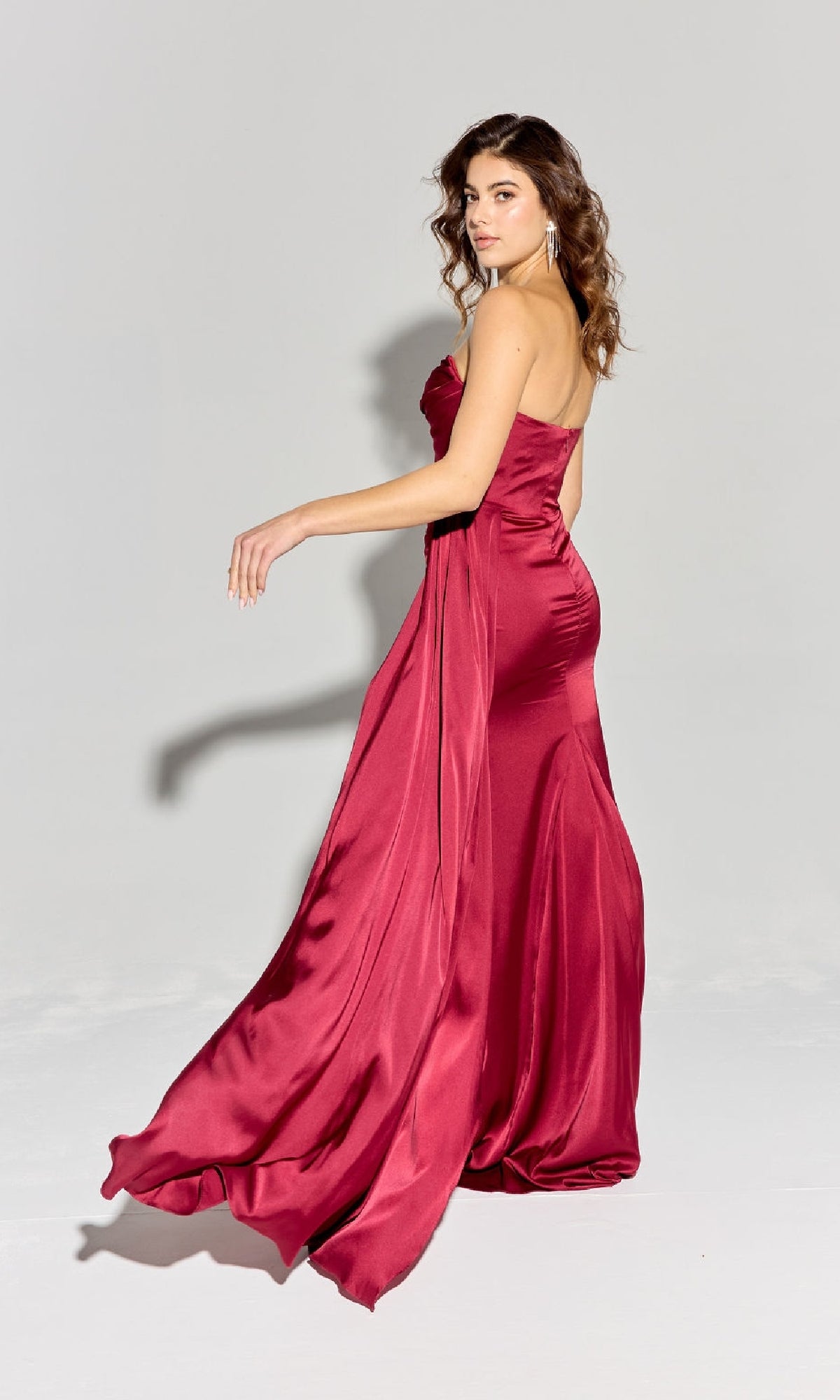 A woman models the Eureka EK118 Strapless Long Satin Prom Dress, posing against a plain light background with her hair in loose waves as she looks over her shoulder.