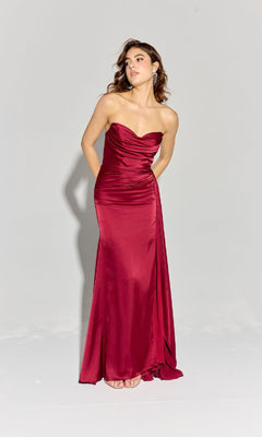 A woman stands against a plain light gray background wearing the Strapless Long Satin Prom Dress: Eureka EK118, a fitted, floor-length red evening gown.