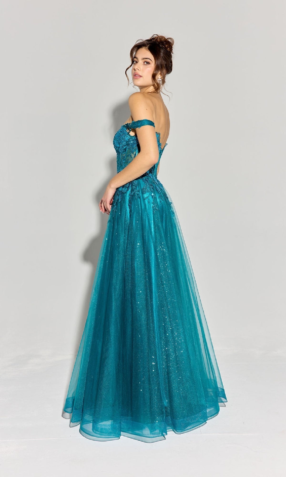 A woman stands slightly turned, modeling the Eureka EK128 Off-Shoulder Long Prom Ball Gown in teal, featuring a corset-style bodice and a glitter-adorned floor-length lace tulle skirt against a plain light background.