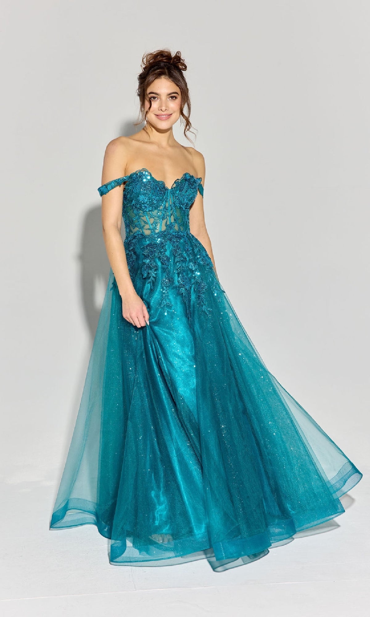 A woman wears the Eureka EK128 Off-Shoulder Long Prom Ball Gown in teal, featuring a corset-style bodice with sheer accents and a full lace tulle skirt, standing against a plain light background.