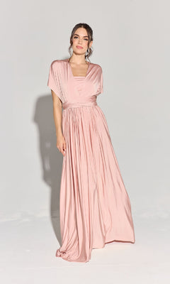 A woman stands against a plain background wearing the Eureka EK145 Multi-Way Long Pink Prom Dress with short sleeves and a draped, pleated skirt.