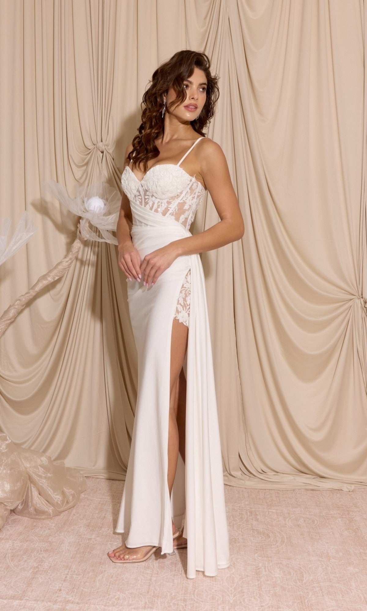 A woman in the Long Prom Dress: Eureka EK166, featuring lace details, a thigh-high slit, and a sheer-embroidered bodice, stands before beige draped curtains.