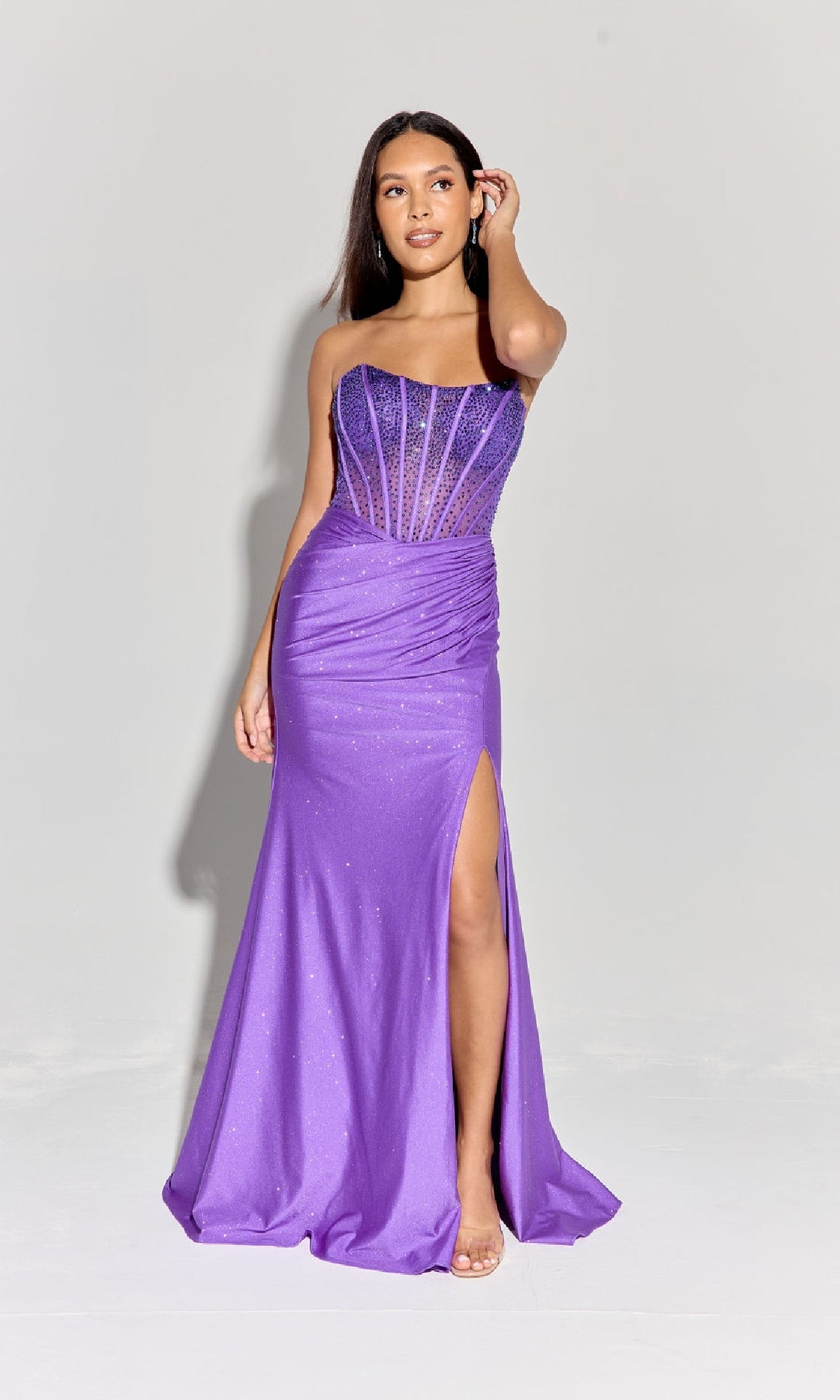 A woman stands against a light background wearing the Strapless Beaded Long Prom Dress: Eureka EK169, featuring a purple floor-length skirt, thigh-high slit, sheer corset bodice, and subtle sparkly details.