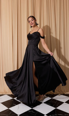 A woman in the Eureka EK176 long black satin prom dress with a high slit poses indoors on a black-and-white checkered floor before beige curtains.