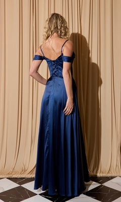 A woman with curly blonde hair stands with her back to the camera on a checkered floor, wearing the Eureka EK176 long satin prom dress in deep blue, set against beige drapes.