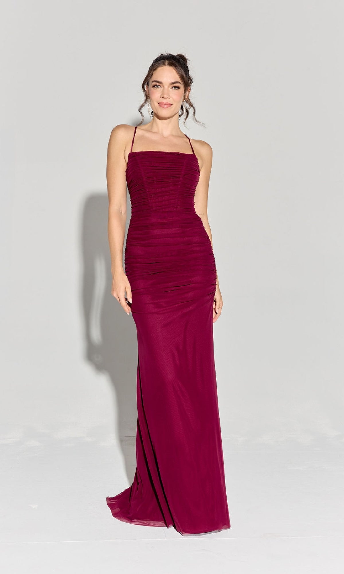 A woman models the Eureka EK177 Strappy-Back Slinky Long Prom Dress, a sleeveless, floor-length fitted burgundy gown with thin straps, against a plain light background.