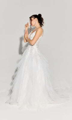 A woman in profile wears the Eureka EK188 Ruffled Long Glitter Prom Ball Gown, featuring a sleeveless white design with lace and tulle, standing elegantly against a plain light background.