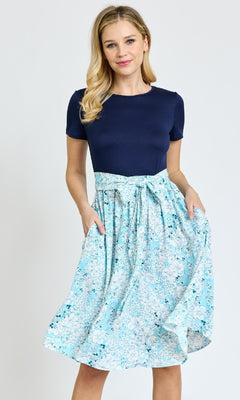 A woman stands wearing a Knee-Length Floral Casual Dress with Pockets, holding the skirt with one hand.