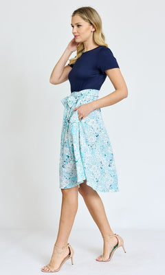 Woman wearing a Knee-Length Floral Casual Dress with Pockets in light blue, paired with beige heels, walking against a plain white background.