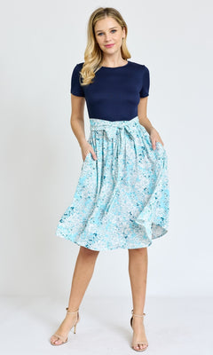 Woman stands against a plain background, wearing the Knee-Length Floral Casual Dress with Pockets in navy blue, paired with nude heels.