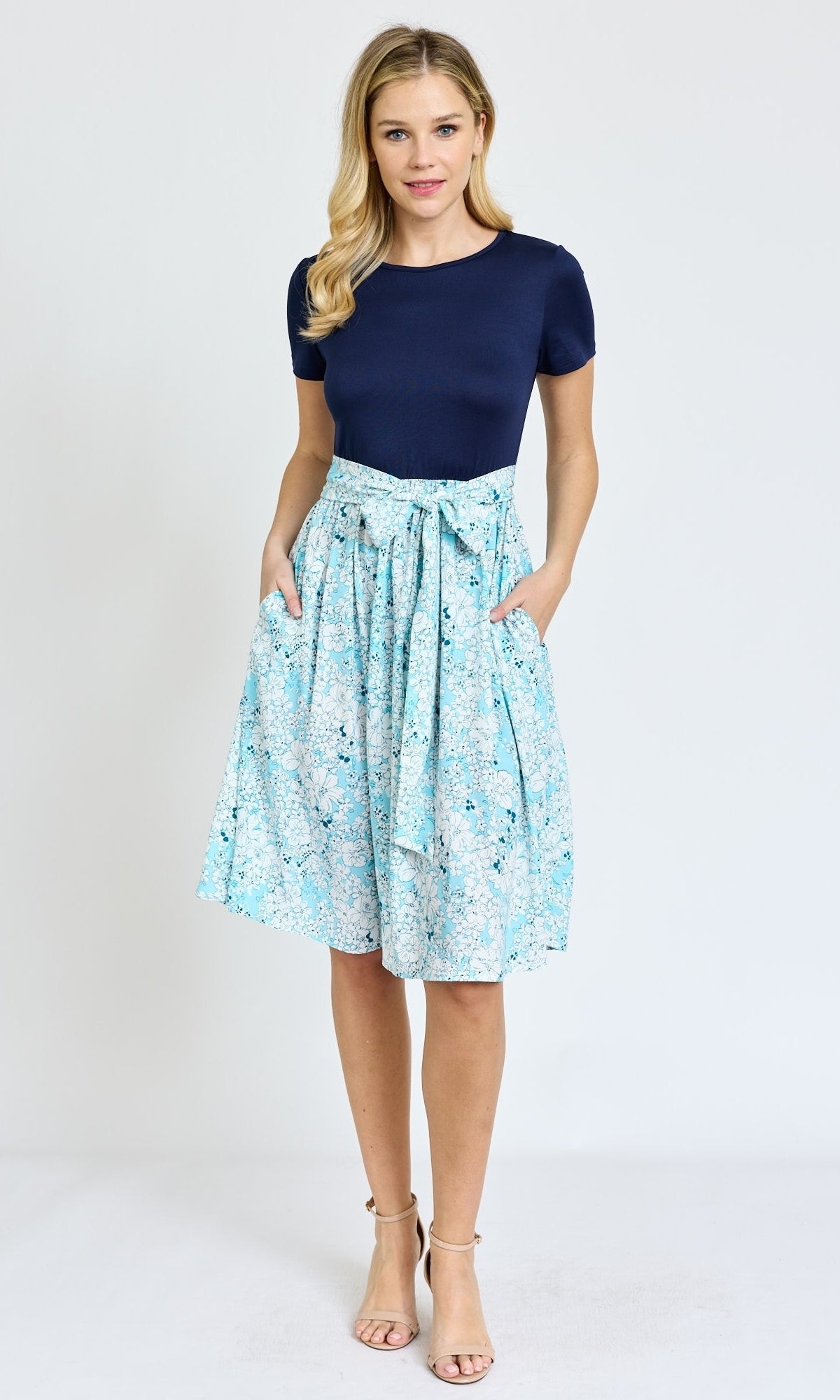 A woman stands against a plain background wearing the Knee-Length Floral Casual Dress with Pockets, styled with nude heeled sandals.