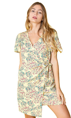 A woman wears the Floral Print Casual Short Wrap Dress, featuring short sleeves, a yellow floral design, v-neckline, and side tie—ideal for a casual look against a white background.