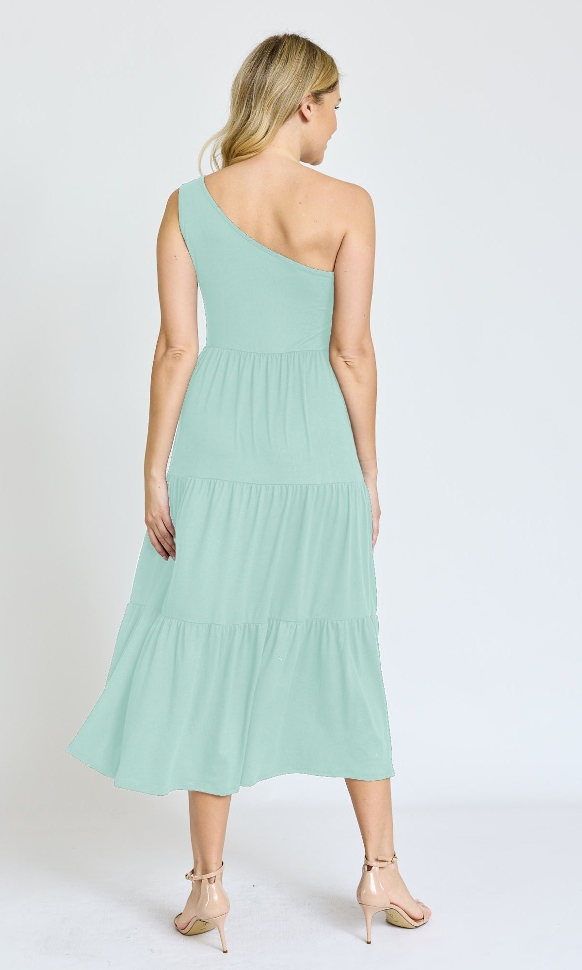 A woman faces away, wearing the One-Shoulder Casual Everyday Midi Dress in light green with tiered midi length and nude heels, set against a plain white background.