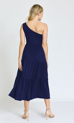 A woman faces away, wearing the One-Shoulder Casual Everyday Midi Dress in navy blue with tiered midi length and nude ankle-strap heels, set against a plain white background.