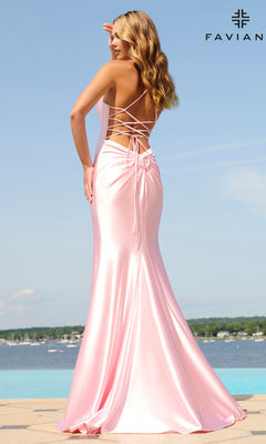 A woman stands outdoors by the water in a shiny pink Statement-Back Long Prom Dress (Faviana ES10890) featuring lace-up detailing and a mermaid skirt. The "FAVIAN" logo is visible in the top right corner.
