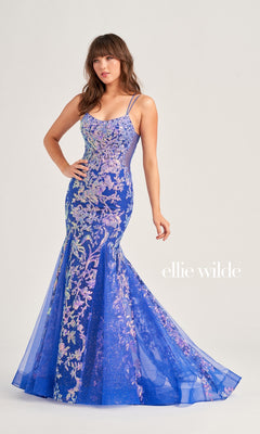 A woman wears the Ellie Wilde Sequin Long Mermaid Prom Dress EW35008, a fitted blue mermaid gown with floral embroidery and spaghetti straps, standing against a plain background. "ellie wilde" is displayed on the right.
