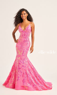 A woman models the Ellie Wilde Long Tulle Designer Prom Dress EW35011—a fitted, floor-length pink and gold sequin floral gown with thin straps—standing against a light background, with "ellie wilde" text visible.
