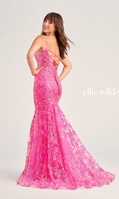 A woman models the Ellie Wilde Designer Glitter Prom Dress EW35013, a bright pink, floor-length, sequin mermaid gown with thin straps and a lace-up back, set against a plain background.