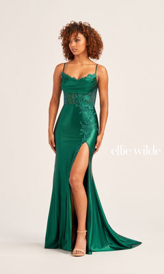A woman stands against a plain background in the Ellie Wilde Choker Designer Prom Dress EW35028—an emerald green gown with beaded-lace floral appliques, spaghetti straps, a thigh-high slit, and “ellie wilde” text beside her.