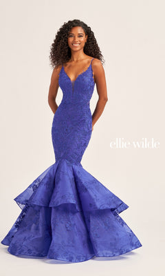A woman models the Ellie Wilde Long Lace Mermaid Prom Dress EW35038, featuring a fitted deep blue silhouette with beaded lace and tiered ruffle hem. The "ellie wilde" logo appears on the right against a plain background.