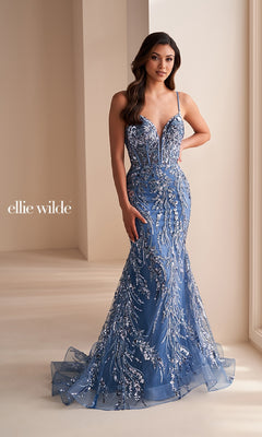 Woman wearing the Ellie Wilde Long Black Sequin Prom Dress EW35039, a floor-length mermaid gown with sleeveless design and silver sequin embellishments, standing indoors near a window. "Ellie Wilde" logo on the left side.
