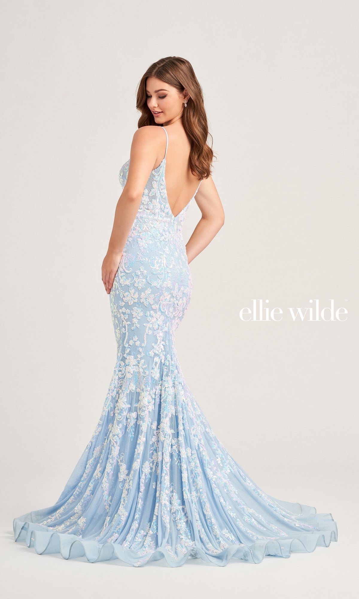 A woman models the Ellie Wilde Long Mermaid Designer Dress EW35048, featuring light blue sequins, floral lace, and a low back, against a plain background. 