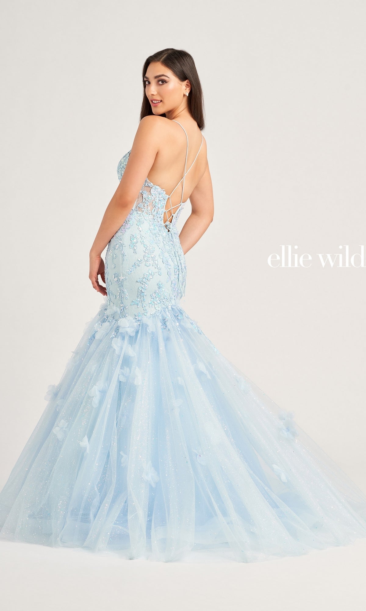 A woman models the Ellie Wilde Designer Mermaid Prom Dress EW35080, a light blue strapless gown with lace details and a tulle skirt, posing with her back slightly turned. 