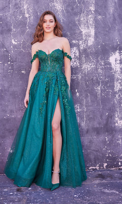 A woman stands against a textured gray wall, wearing the Ellie Wilde Off-Shoulder Long Prom Dress EW35101 in emerald green, featuring floral embellishments and a thigh-high slit.