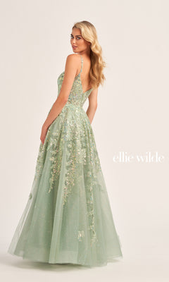 A woman in a pale green Glitter-Tulle Ellie Wilde Long Prom Dress EW35114 with a fitted bodice and thin straps stands slightly turned, highlighting the embellished back and elegant floral appliqué details.