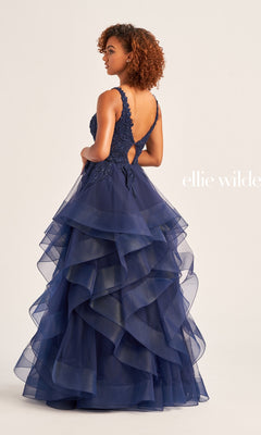 A woman in the Ellie Wilde Tiered Long A-Line Prom Dress EW35119, featuring a lace bodice and open back, stands facing slightly away from the camera.