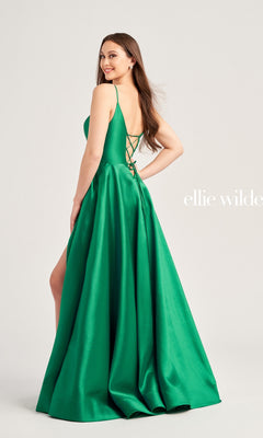 A woman smiles over her shoulder, wearing the Ellie Wilde Long A-Line Satin Prom Dress EW35232 in emerald green satin, featuring a lace-up strappy back and a stylish side slit.